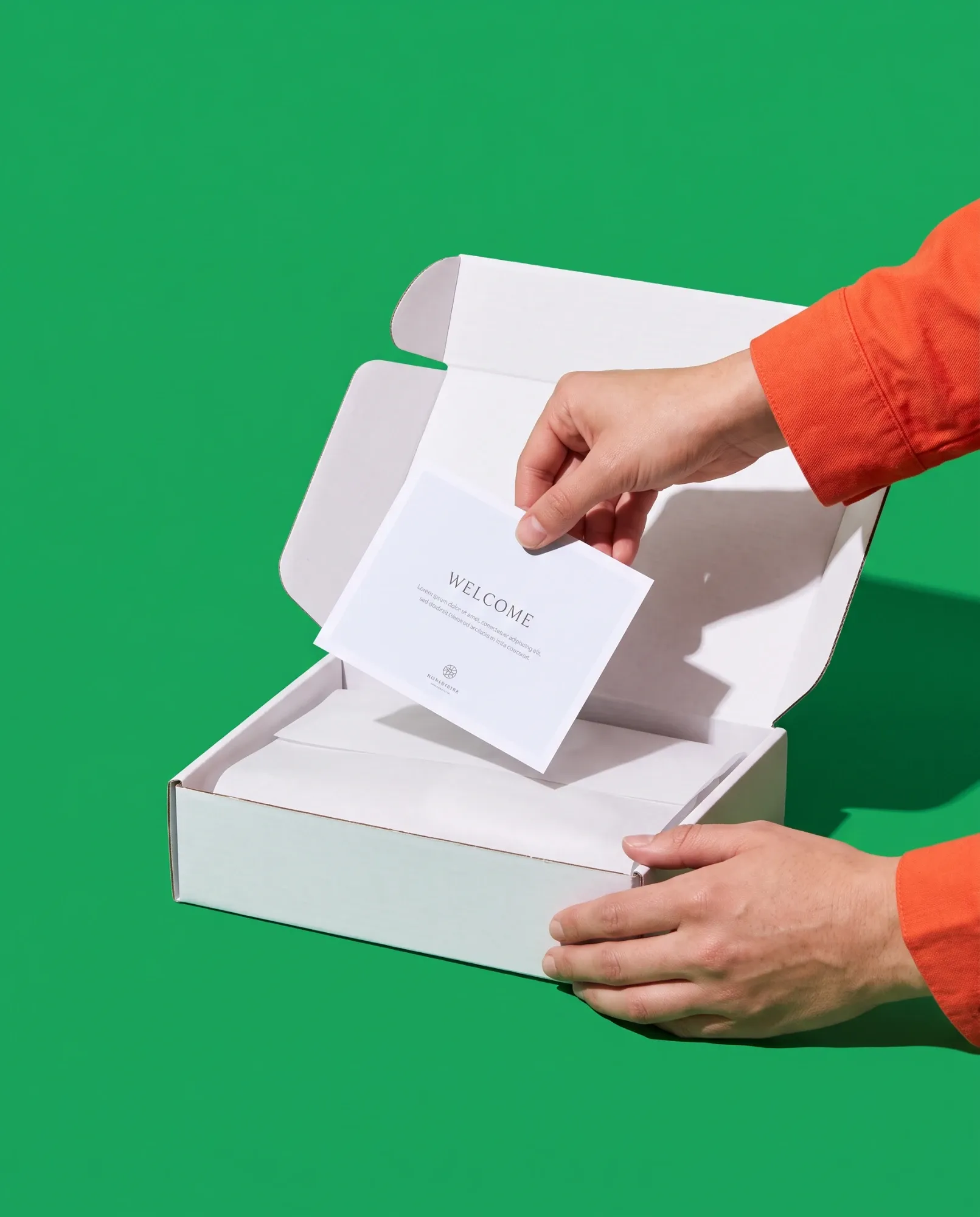 Hands placing a printed welcome card into a white mailer box on a green background